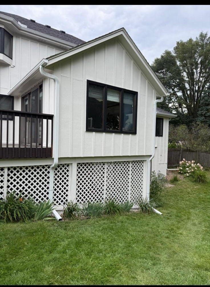 A painted addition in cream board-and-batten with black window trim and white lattice skirting below the deck.