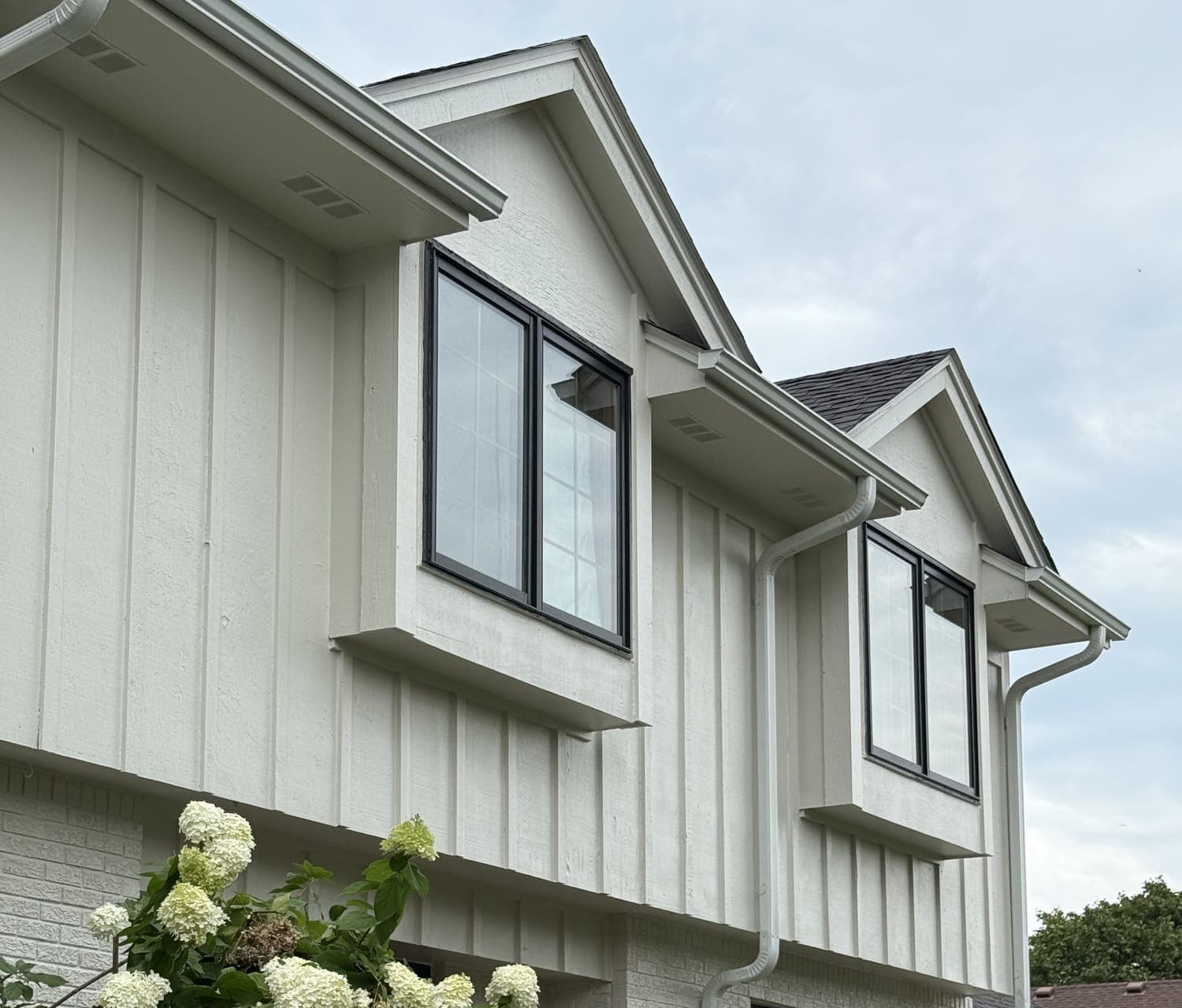 Cream board-and-batten gables with black window frames, photographed from below against an overcast sky.