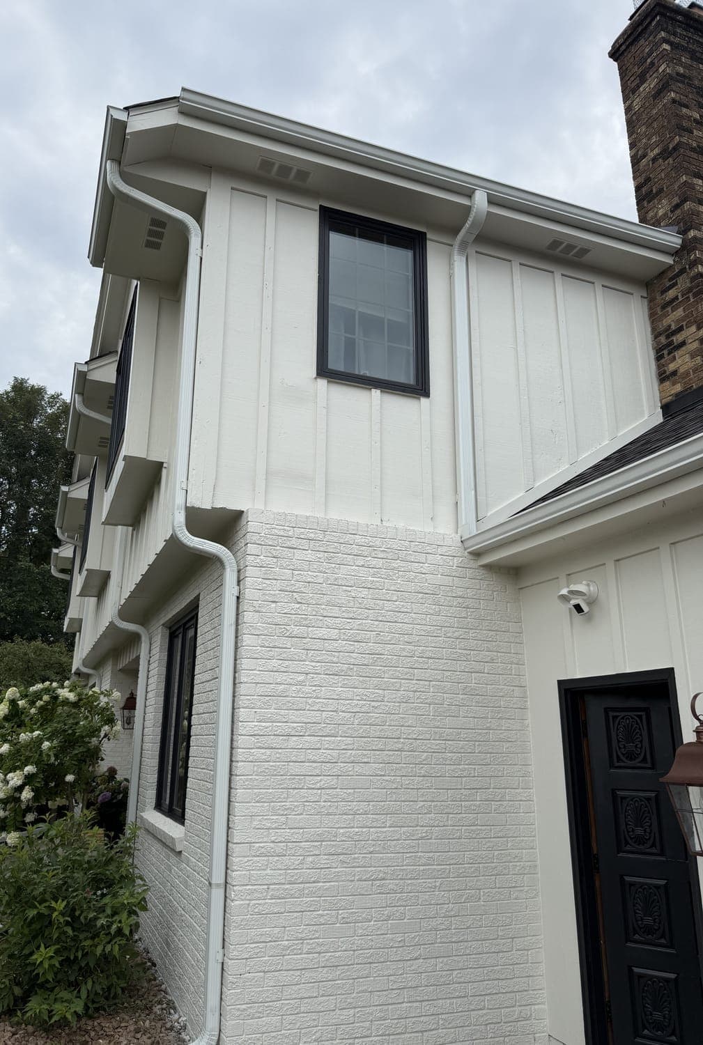 A Twin Cities home after an exterior repaint: painted white brick, white board-and-batten siding, black window frames and a black front door.
